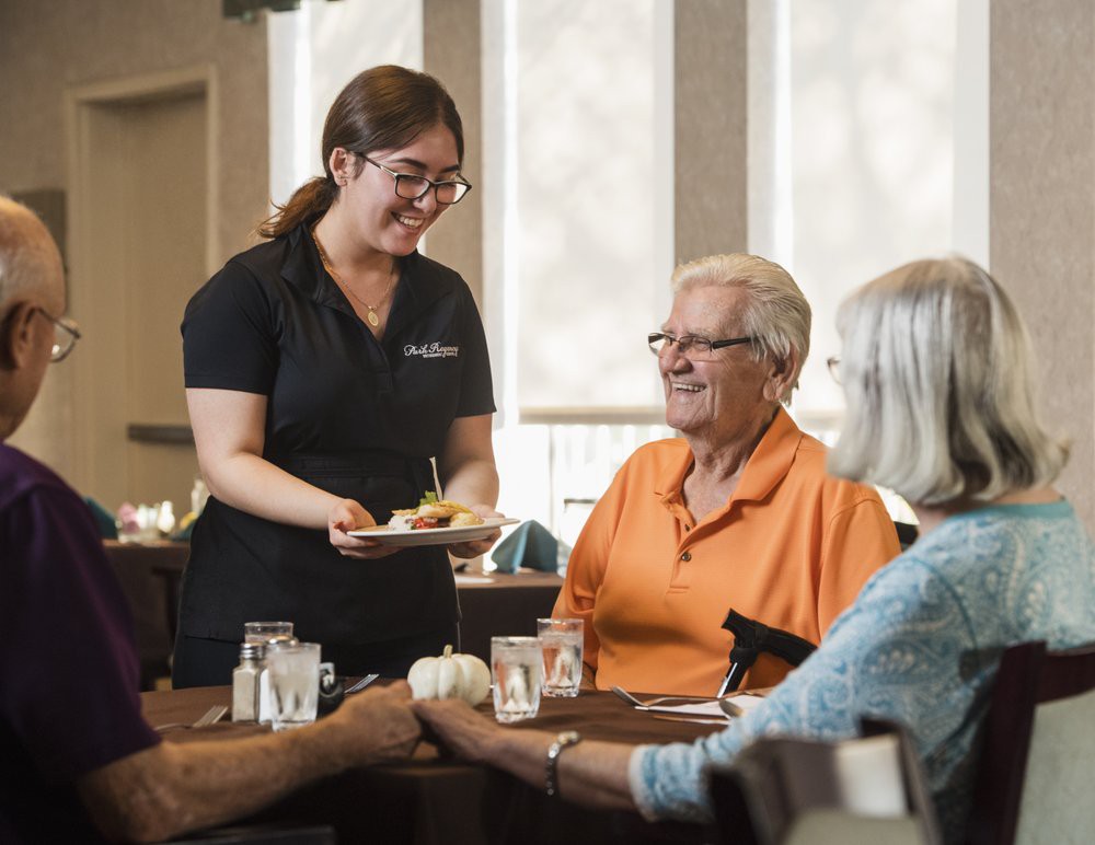 A server greets elderly customers at a restaurant table.