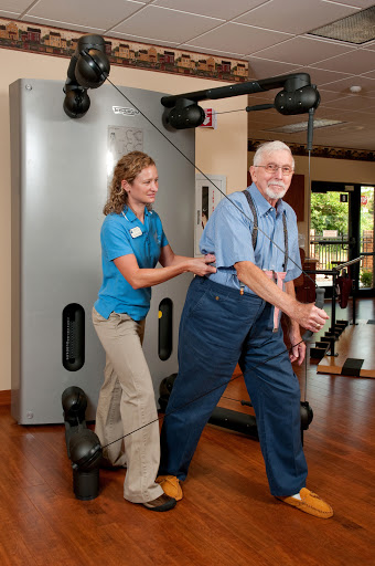 An elderly man receives assistance during a physical training session at a fitness center.