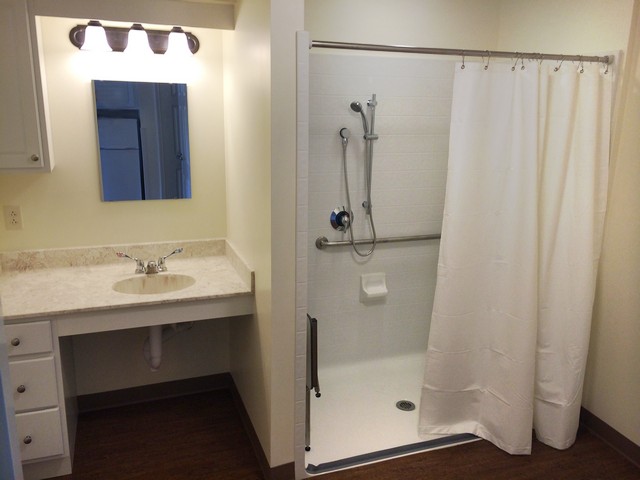 An accessible bathroom featuring a sink, mirror, and shower with a curtain.