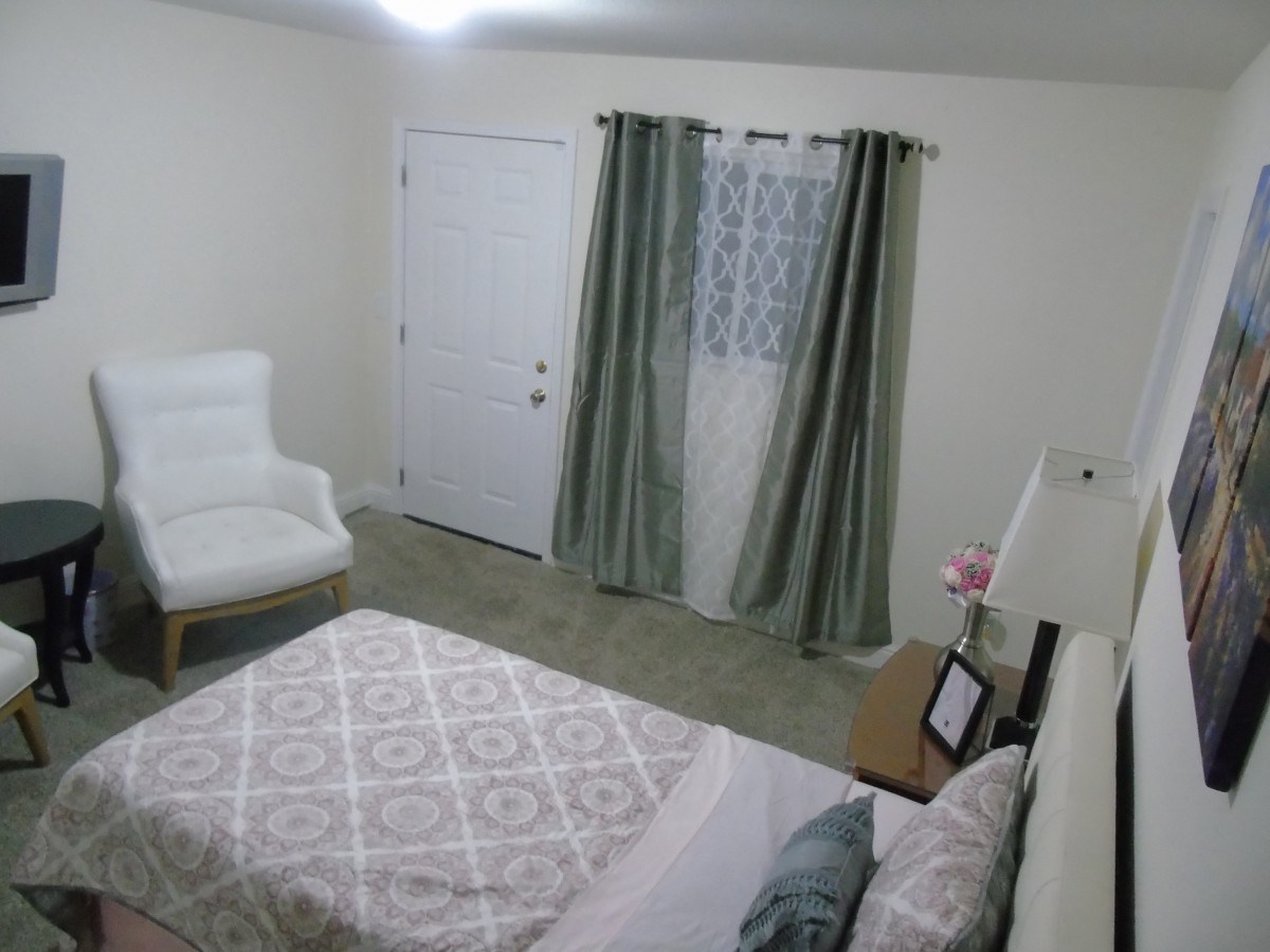 A cozy bedroom with a neatly made bed, white chair, and elegant curtains.