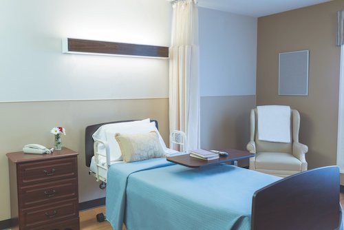 A clean and organized hospital room with a single bed and chair.