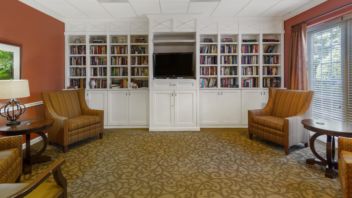 A cozy library with built-in bookshelves, a TV, and two armchairs.