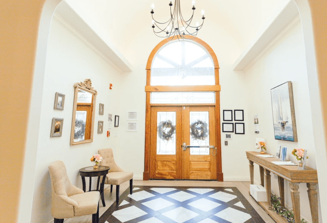 A beautifully decorated foyer with a grand wooden front door, a chandelier, and elegant furnishings.