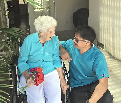A warm moment shared between an elderly woman in a wheelchair and a man, as they engage in a heartfelt conversation with flowers in hand.