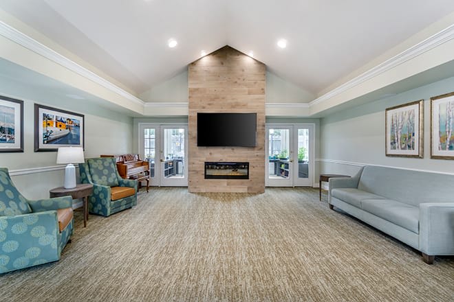A modern living room featuring a central fireplace with a mounted television, surrounded by comfortable seating and a vaulted ceiling.