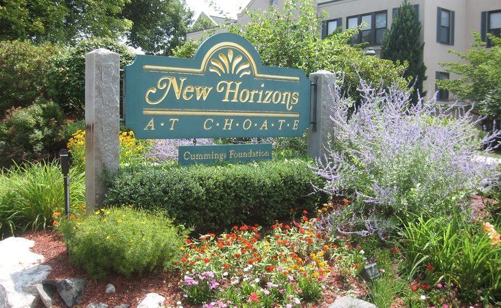 Entrance sign for New Horizons surrounded by lush landscaping and colorful flowers.