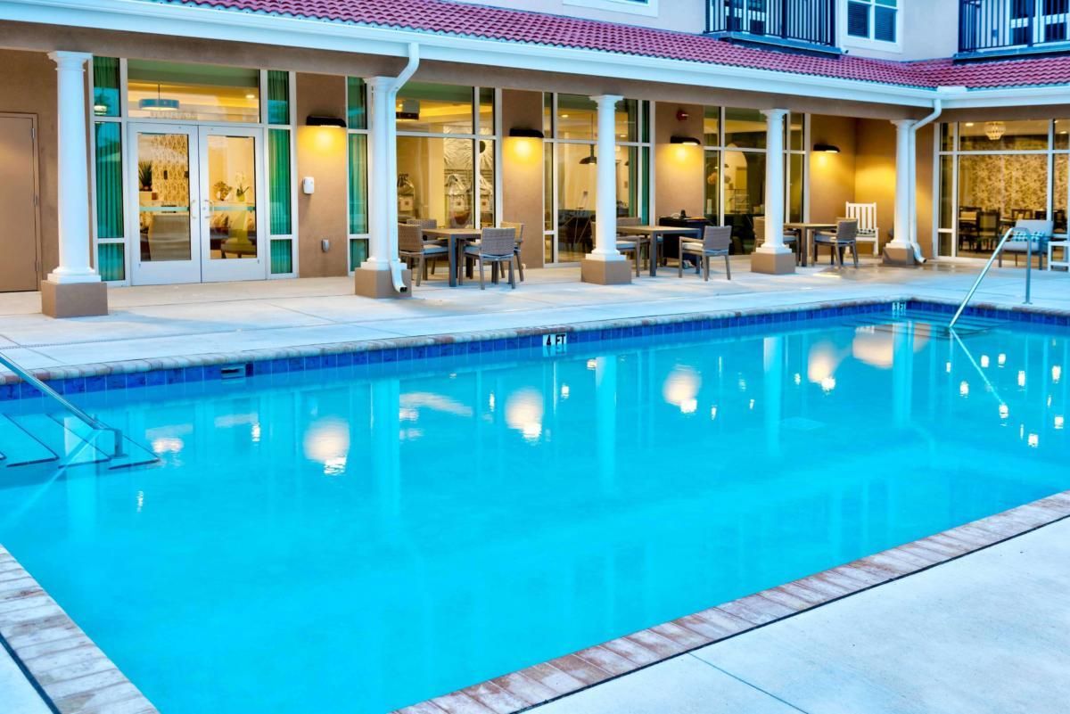 A serene outdoor hotel swimming pool with seating area and lighting in the evening.