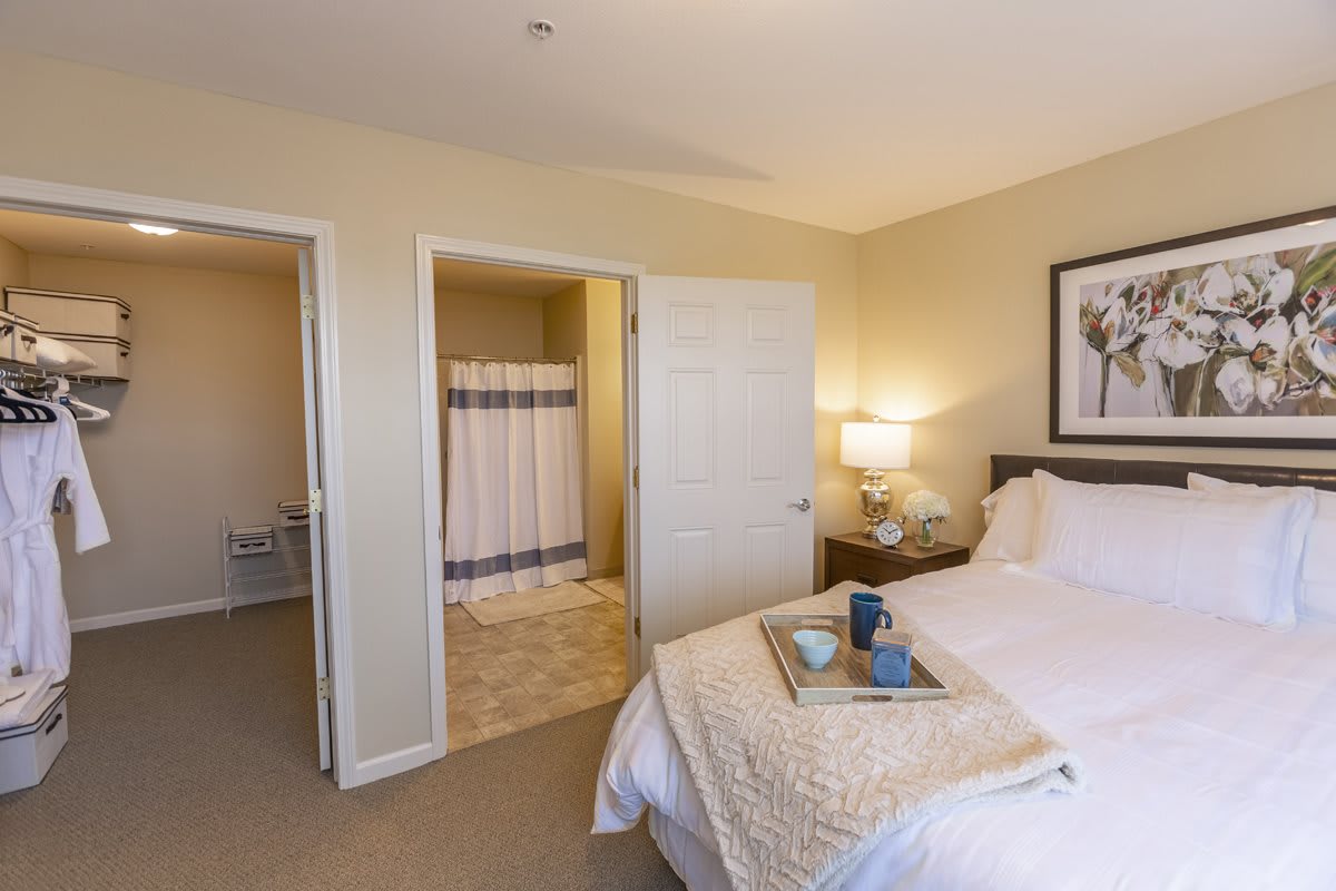 A cozy bedroom featuring a neatly made bed, adjacent nightstand with a lamp, and an open door leading to a bathroom.