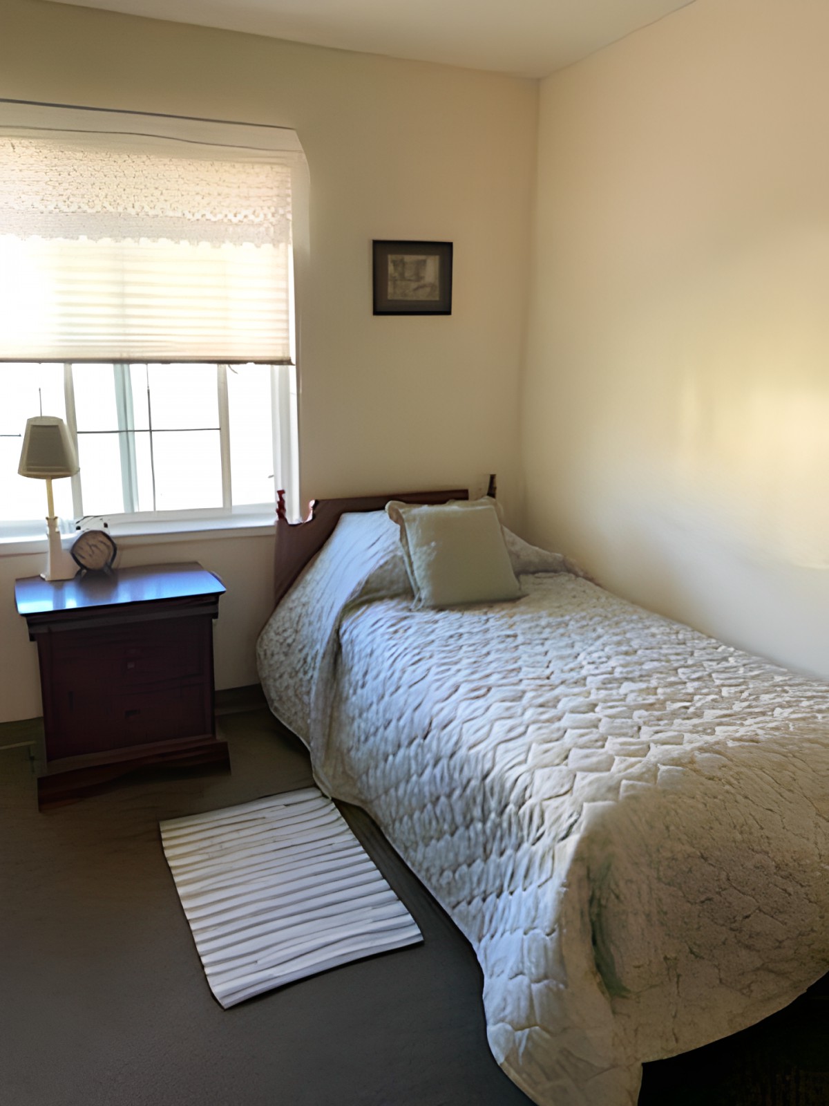 A cozy, minimalist bedroom with a single bed and a nightstand next to a window.