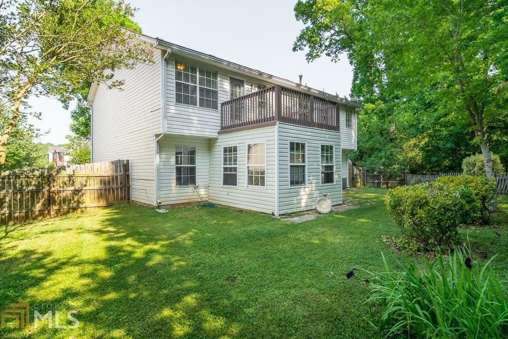 A two-story house with a green backyard surrounded by trees.