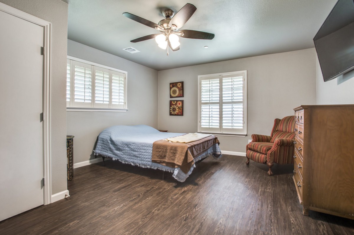 A minimalist bedroom featuring wood flooring, a ceiling fan, and an armchair next to the bed.