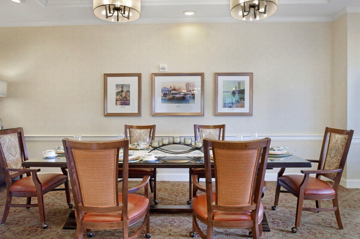 A neatly arranged dining room with a glass table, surrounded by wooden chairs and adorned with framed art on the walls.
