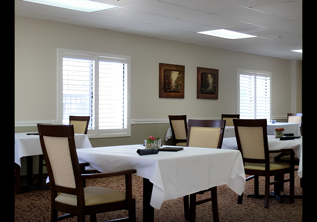 A neatly arranged dining room with tables and chairs, accompanied by paintings on the wall and large windows.