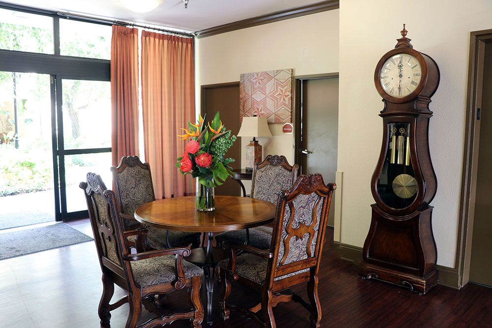 A cozy dining room with antique furniture, featuring a round wooden table surrounded by ornate chairs and decorated with a vase of vibrant flowers.