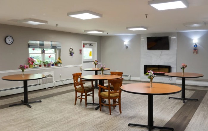 A modern dining space featuring round tables, wooden chairs, and a TV mounted above a fireplace.
