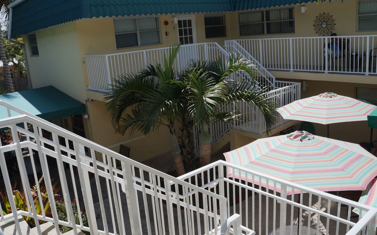 A sunny courtyard with a palm tree, balconies, and an umbrella.