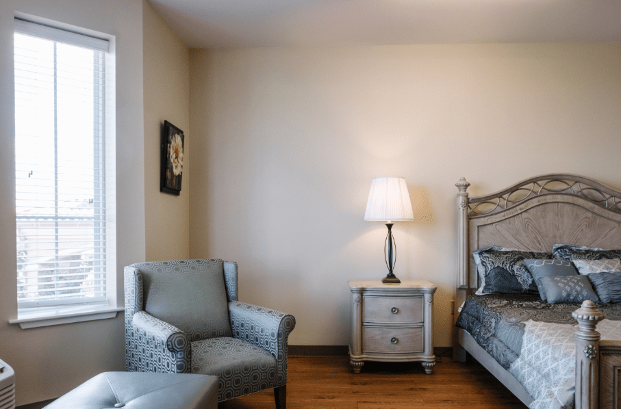 A cozy bedroom with a comfortable chair, nightstand, and lamp.