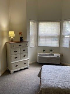 A cozy bedroom corner featuring a chest of drawers, a lamp and a large window with blinds allowing in daylight.