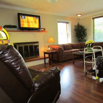 A cozy living room featuring a large sofa, TV mounted above the fireplace, and a walker for mobility assistance.