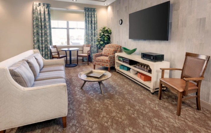 A cozy living room with a sofa, armchairs, and a large television on the wall.