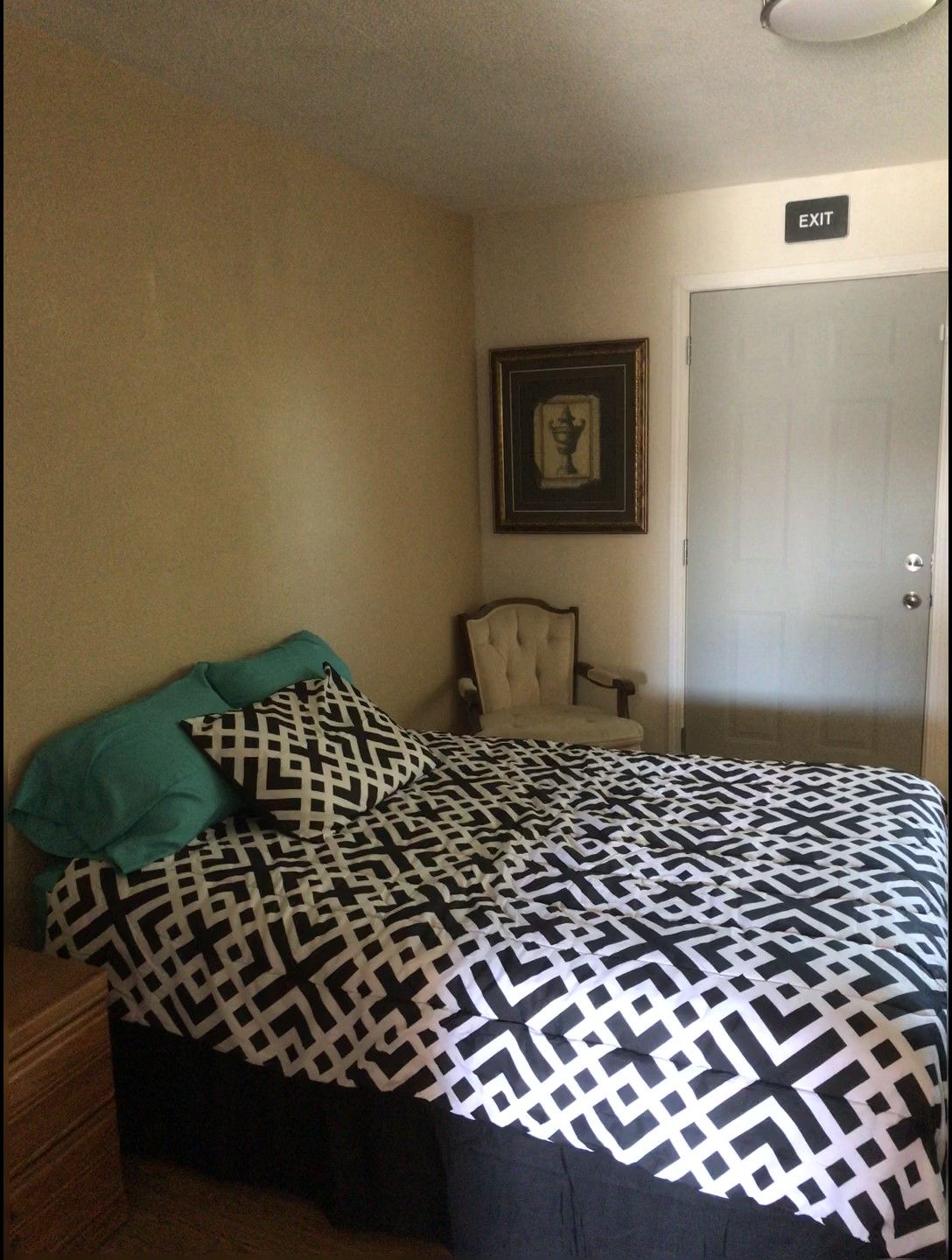 A cozy bedroom with a patterned bedspread, chair, and wall art.