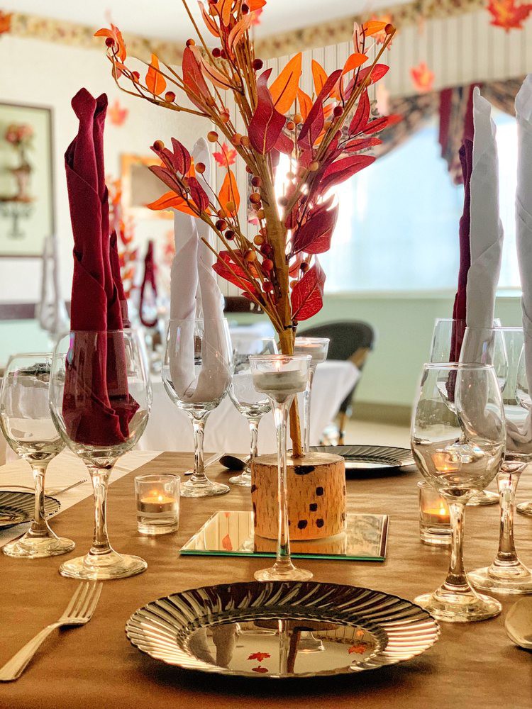 An elegantly set dining table with an autumn-themed centerpiece and neatly arranged glassware and napkins.