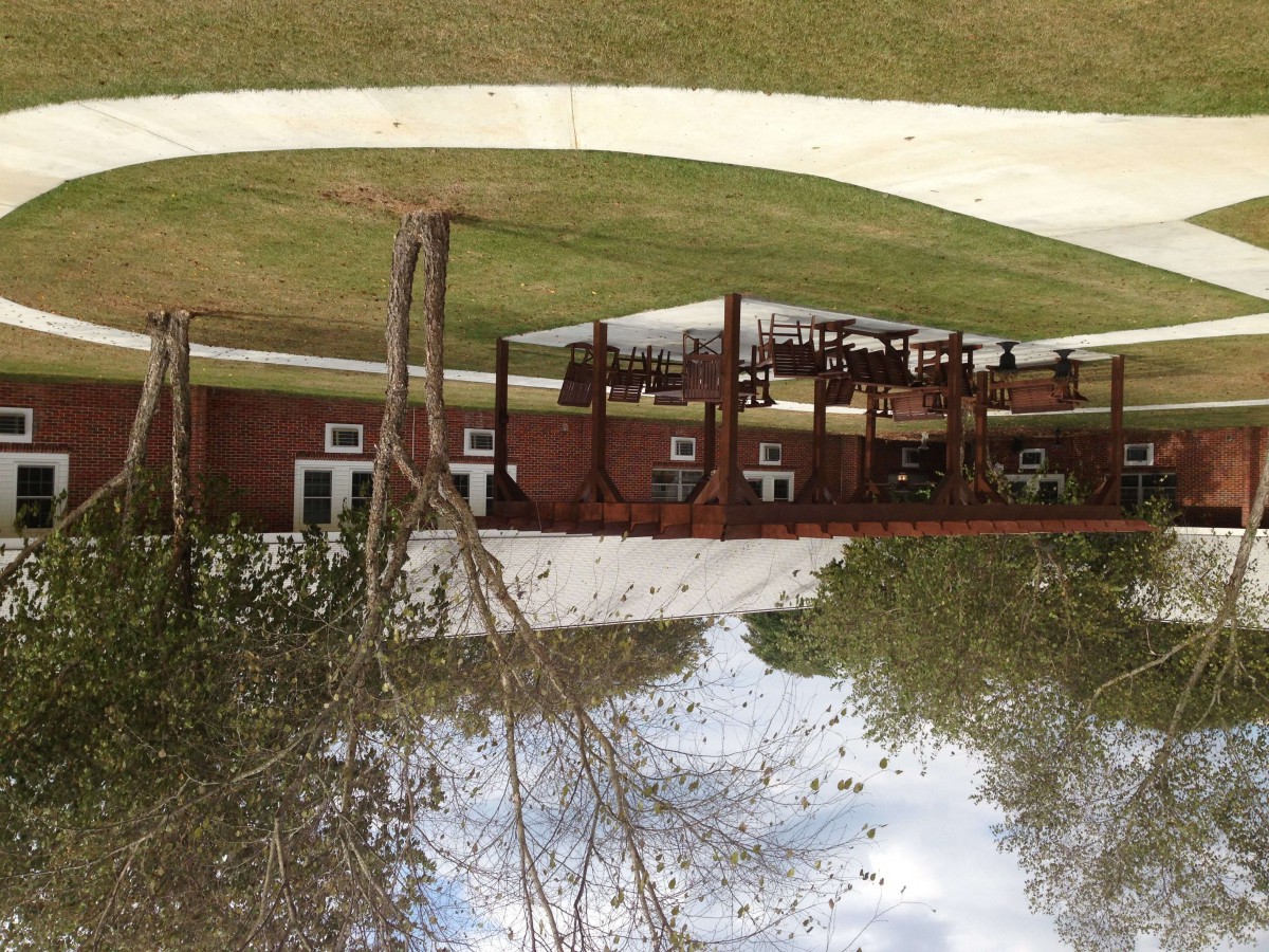 A building reflected in a body of water surrounded by grass and trees.