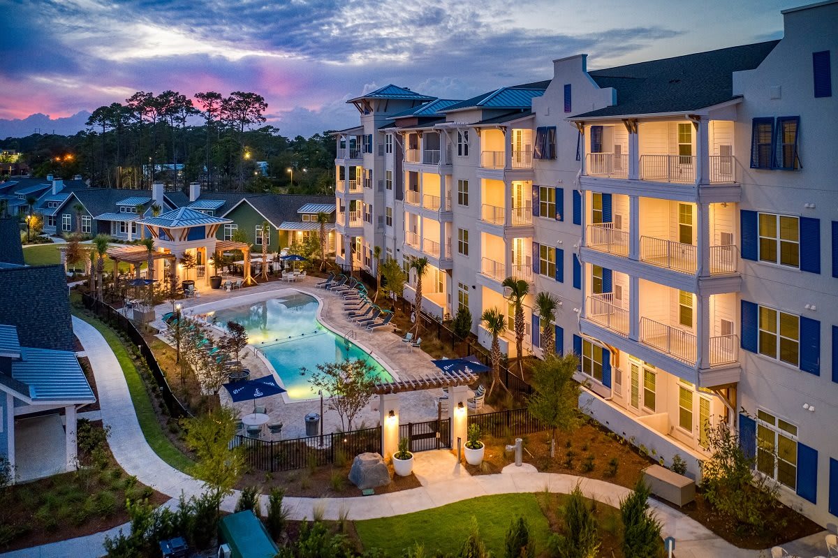 An illuminated apartment complex with a swimming pool at dusk.