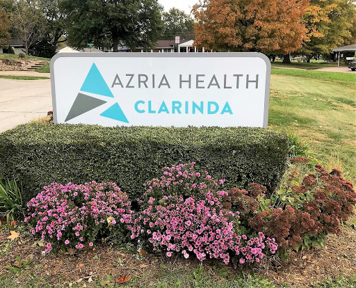 Signage for Azria Health in Clarinda, surrounded by flowers.