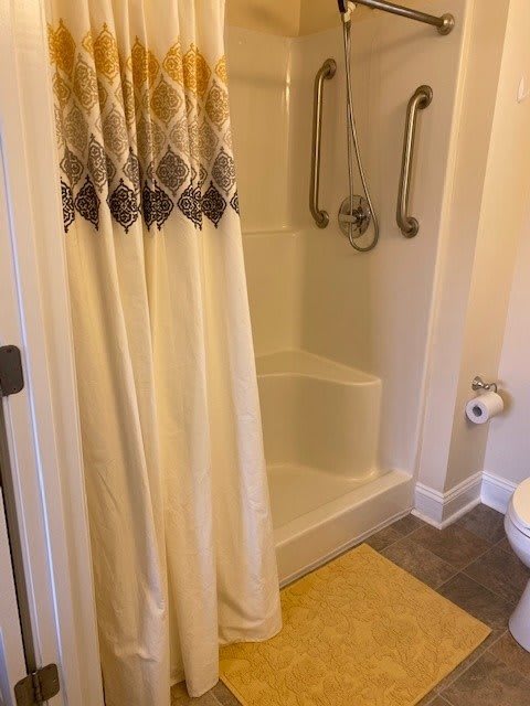 A bathroom with a shower featuring grab bars and a patterned curtain.