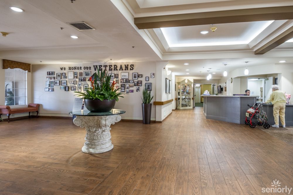 The image shows an inviting lobby with a reception desk, decorated with plants and a wall of photographs honoring veterans.