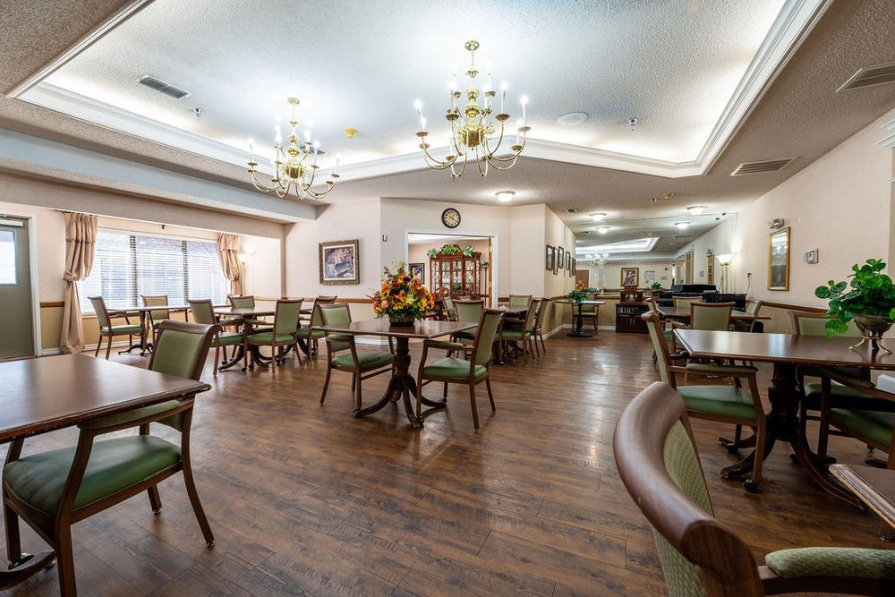 A cozy dining area with elegant chandeliers, wooden flooring, and neatly arranged tables and chairs.