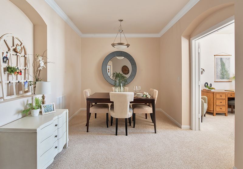 A stylish dining room with a round mirror, a chandelier, and elegant furniture.