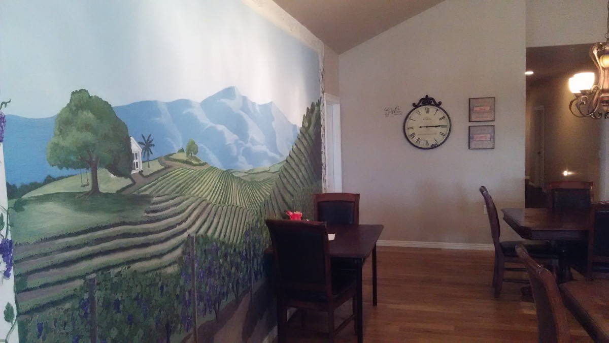A dining room with a mural of mountains and rice terraces on the wall, featuring a small table with two chairs and a clock hanging above.