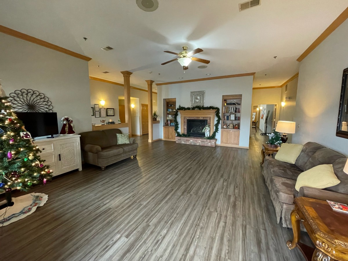 A spacious living room with wood flooring, featuring a fireplace, seating area, ceiling fan, and built-in bookshelves.