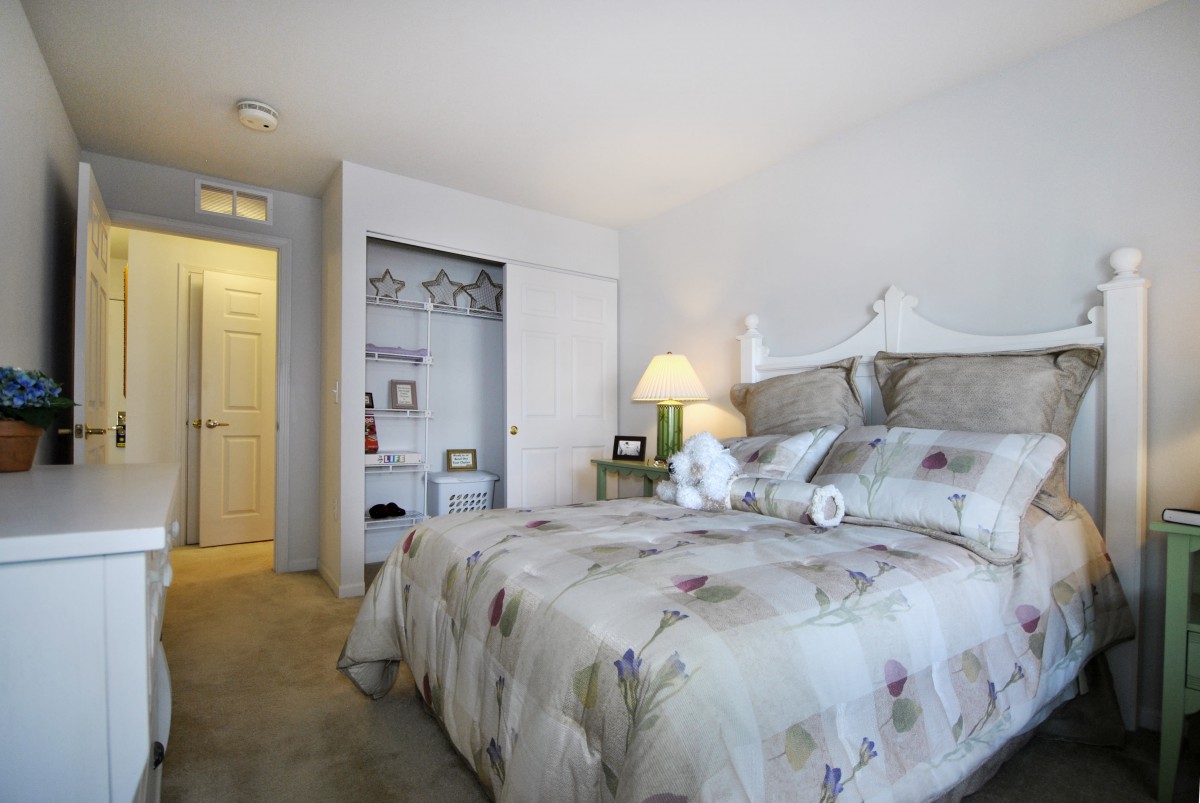 A cozy bedroom featuring a neatly made bed with floral bedding, a bedside lamp, and an open closet.