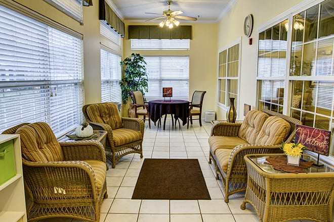 A cozy living room with wicker furniture, a small round table, and large windows.