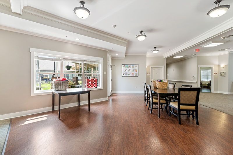 A spacious dining area with wood flooring, featuring a large table and chairs, illuminated by ceiling lights.