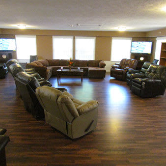 A spacious living room with multiple sofas and recliners arranged in a circle on wooden flooring.