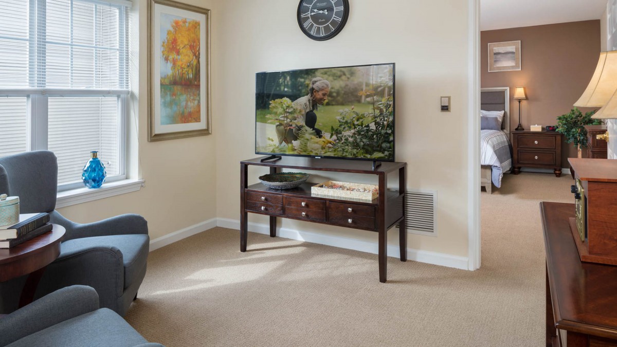 A cozy living room featuring a television on a console table, decorated with a wall clock and artwork.