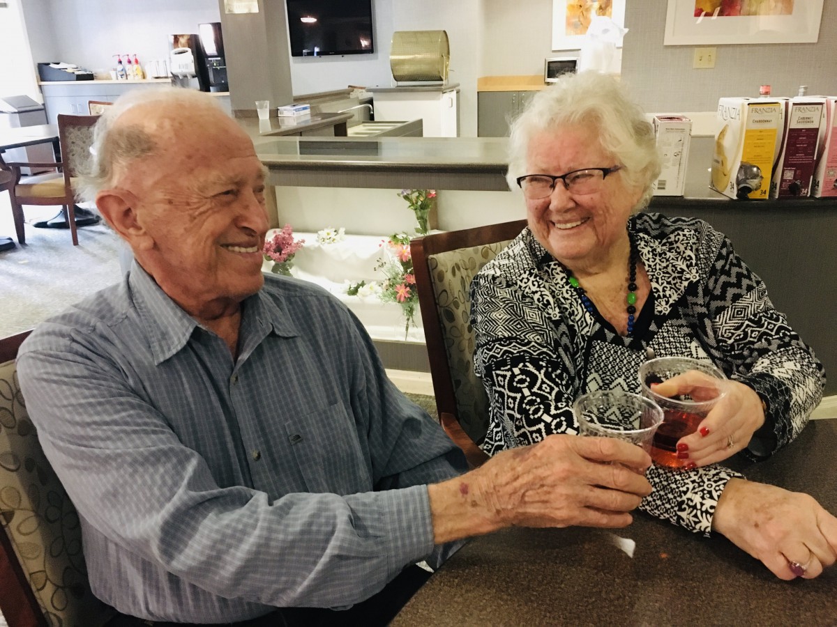 An elderly couple smiling and clinking glasses in a celebratory gesture.