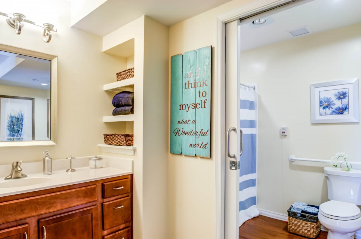 A bathroom with wooden cabinets, open shelves holding towels, and wall art decor.