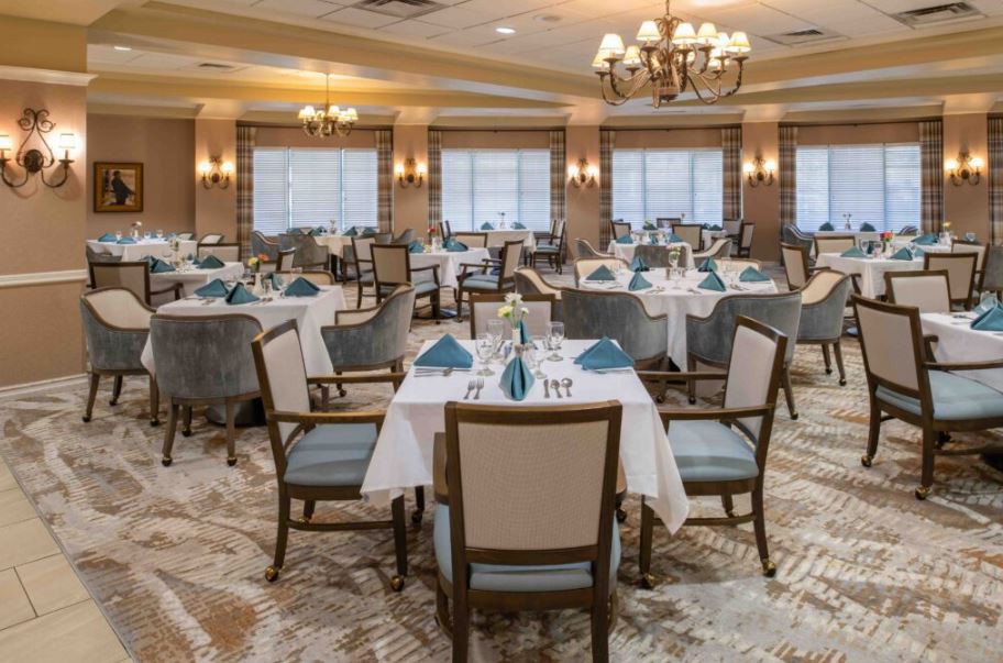 An elegant dining room with neatly arranged tables and chairs, featuring chandeliers and soft lighting.