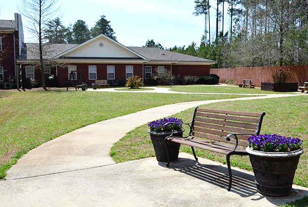 A peaceful garden setting with a bench and a pathway leading to a brick building.