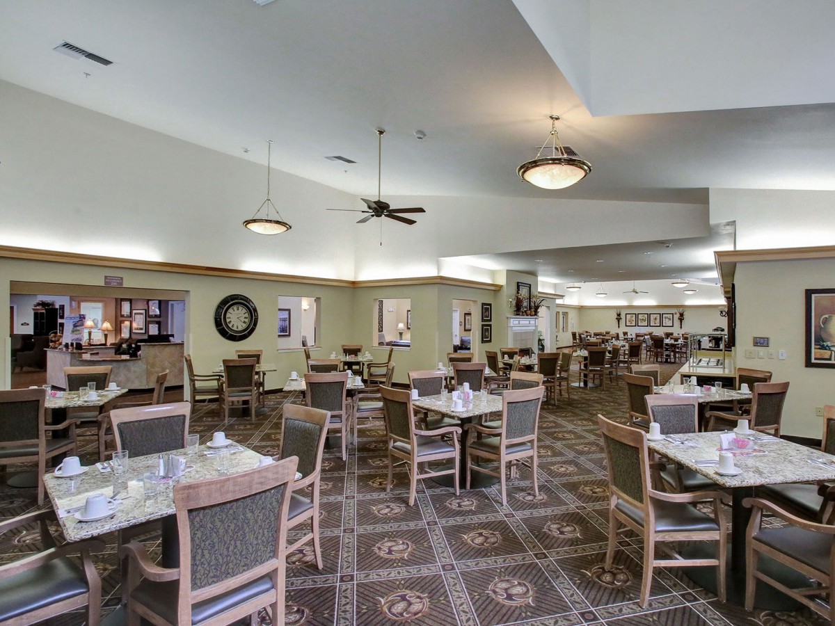 An empty dining area with neatly arranged tables and chairs, featuring ceiling lights and a patterned carpet floor.