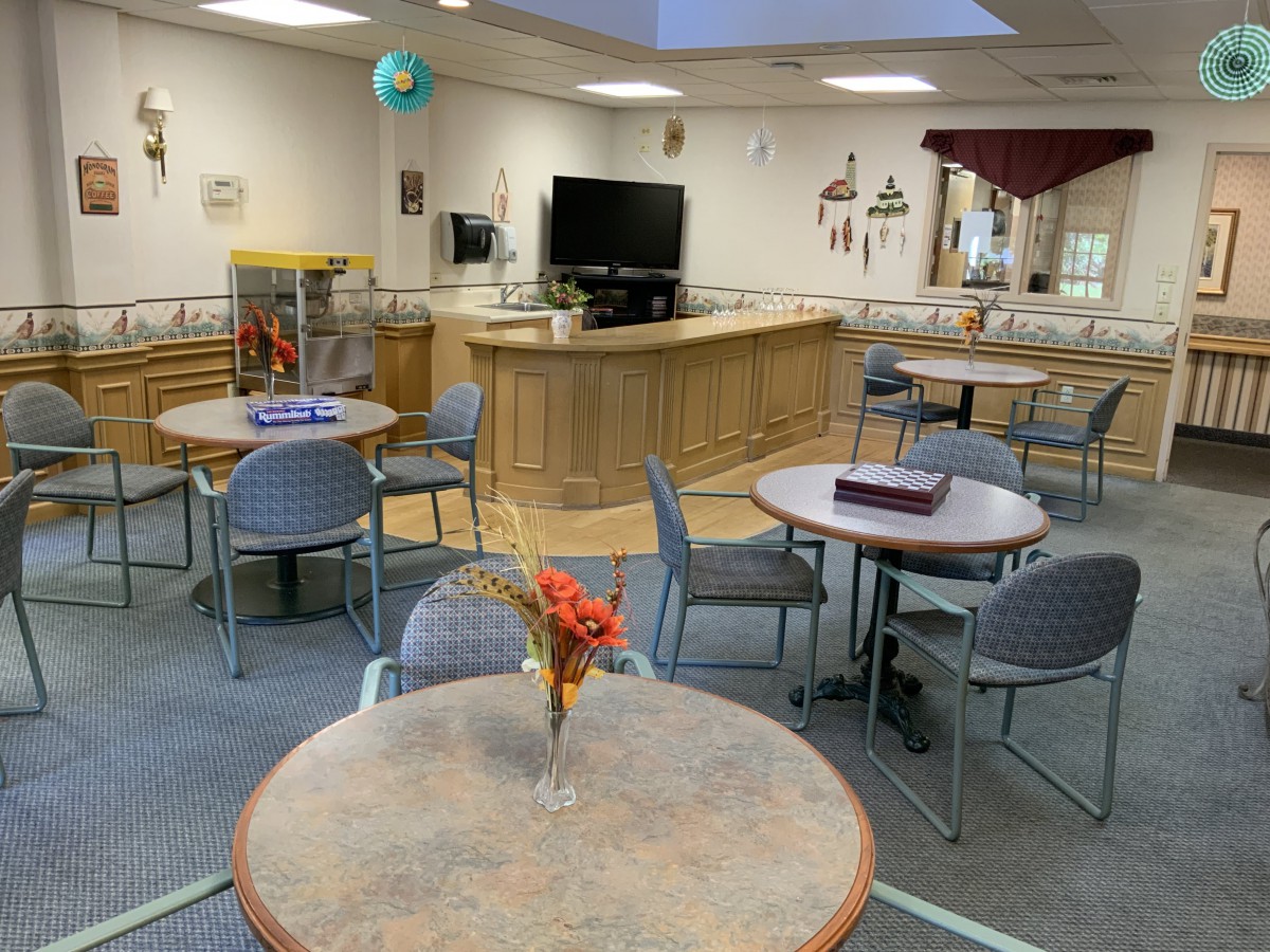 A cozy dining area with several round tables and chairs, a television, and decorative elements including a flower vase on one of the tables.