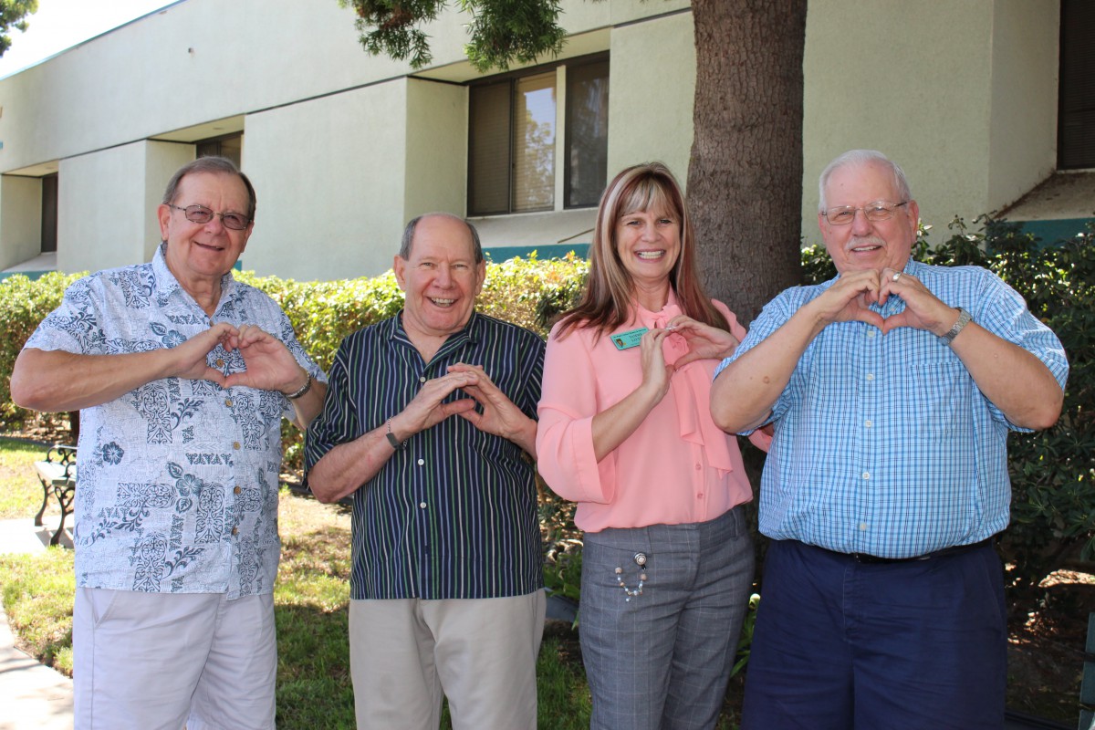A group of four people standing outside, making heart shapes with their hands and smiling.