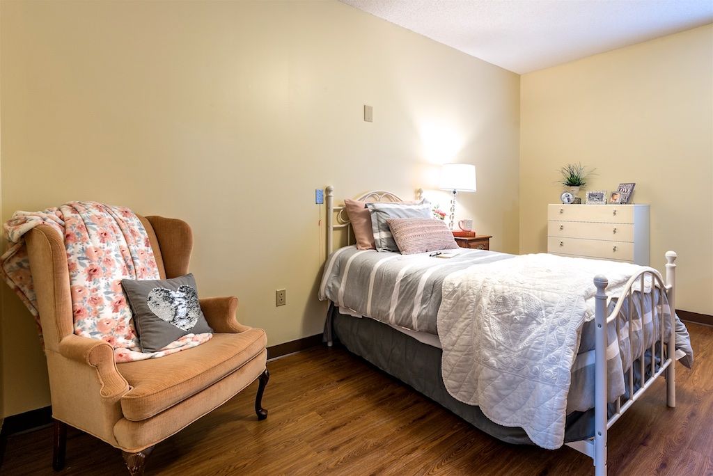 A cozy bedroom with a neatly made bed, armchair, and a dresser.