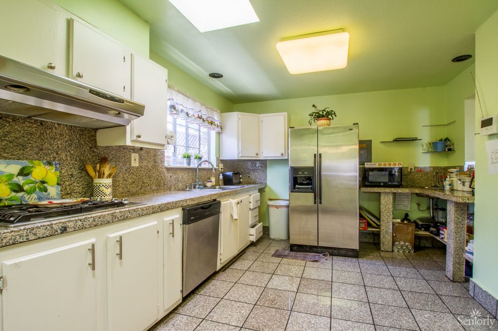 A brightly lit kitchen with green walls, featuring white cabinets and a stainless steel refrigerator.