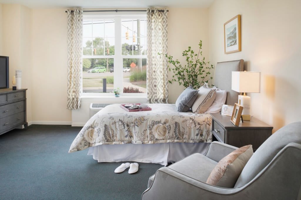 A cozy bedroom with a neatly made bed, elegant decor, and ample natural light streaming through large windows.